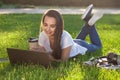 Young woman using laptop in the park lying on the green grass. Leisure time activity concept. Royalty Free Stock Photo