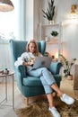 Young woman using laptop sitting in armchair, remote work at home Royalty Free Stock Photo