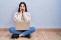 Young woman using laptop sitting on the floor at home afraid and shocked, surprise and amazed expression with hands on face Royalty Free Stock Photo