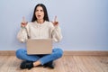 Young woman using laptop sitting on the floor at home amazed and surprised looking up and pointing with fingers and raised arms Royalty Free Stock Photo