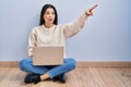 Young woman using laptop sitting on the floor at home pointing with finger surprised ahead, open mouth amazed expression, Royalty Free Stock Photo