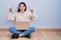 Young woman using laptop sitting on the floor at home smiling amazed and surprised and pointing up with fingers and raised arms Royalty Free Stock Photo