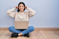 Young woman using laptop sitting on the floor at home smiling pulling ears with fingers, funny gesture Royalty Free Stock Photo