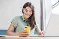 Young woman using laptop and smartphone in office. Beautiful girl texting on phone