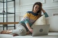 Young woman using laptop, typing, using touchpad, sitting at home on sofa, remote work, work at home