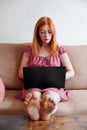 young woman using laptop working from home sitting on couch with feet on table Royalty Free Stock Photo