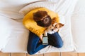 Young woman using mobile phone, cute small dog besides. Sitting on the couch, wearing protective mask. Stay home concept during Royalty Free Stock Photo