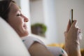 Young woman using mobile phone at home smiling lying in sofa Royalty Free Stock Photo