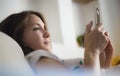 Young woman using mobile phone at home smiling lying in sofa Royalty Free Stock Photo