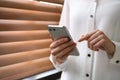 Young woman using modern smartphone near window indoors Royalty Free Stock Photo