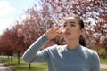 Young woman using nasal drops near blooming trees. Allergy concept