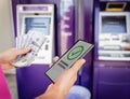 Young woman using the smart phone for cardless withdrawing the cash near the ATM