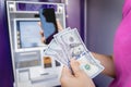 Young woman using the smart phone for cardless withdrawing the cash near the ATM