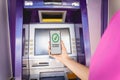 Young woman using the smart phone for cardless withdrawing the cash near the ATM