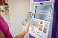 Young woman using the smart phone for cardless withdrawing the cash near the ATM