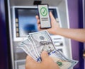 Young woman using the smart phone for cardless withdrawing the cash near the ATM