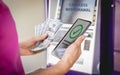 Young woman using the smart phone for cardless withdrawing the cash near the ATM