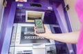 Young woman using the smart phone for cardless withdrawing the cash near the ATM