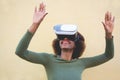 Young woman using virtual reality headset with yellow wall in background - African woman having fun with new trend technology - Royalty Free Stock Photo