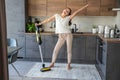 Young woman vacuuming carpet with cordless vacuum cleaner in kitchen and dancing while listening to music Royalty Free Stock Photo