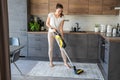 Young woman vacuuming carpet with wireless vacuum cleaner in kitchen. Household and useful technology concept. Royalty Free Stock Photo