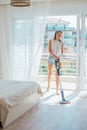 Young woman vacuuming the floor in bright cozy room with cordless vacuum cleaner Royalty Free Stock Photo