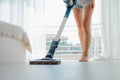 Young woman vacuuming the floor in bright cozy room with cordless vacuum cleaner Royalty Free Stock Photo