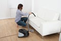 Young woman vacuuming sofa at home