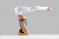 Young woman in variation of salamba sirsasana pose, grey studio