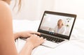 Young woman videoconferencing with her mature mother on webcam, using laptop pc to speak to her parent in bed