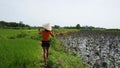 Young woman in Vietnamese cone hat walking in the farm taking selfie video.