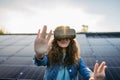 Young woman with virtual goggles on the roof with solar panels.