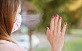 Young woman in virus mask looking sad from the window behind glass pane, touching it with hand. Quarantine or stay at home to be Royalty Free Stock Photo