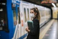 Young woman waits for the subway with a medical mask