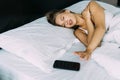 Young woman waking up with mobile alarm clock in her bed Royalty Free Stock Photo