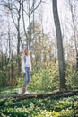 Young woman is walking along a fallen tree in a forest covered with blooming white wood anemones