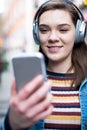 Young Woman Walking Along Street Streaming Music From Mobile Phone