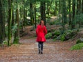 Young woman walking away alone on forest path wearing red long coat