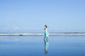 Young woman walking barefoot on empty beach. Full body portrait. Slim Caucasian woman wearing long dress. Enjoy time on the beach