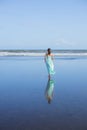 Young woman walking barefoot on empty beach. Full body portrait. Slim Caucasian woman wearing long dress. View from back. Water Royalty Free Stock Photo