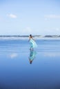 Young woman walking barefoot on empty beach. Full body portrait. Slim Caucasian woman wearing long dress. View from back. Water Royalty Free Stock Photo