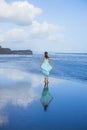 Young woman walking barefoot on empty beach. Full body portrait. Slim Caucasian woman wearing long dress. View from back. Water Royalty Free Stock Photo