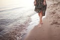 Young woman walking barefoot on surf line, Legs and skirt close up