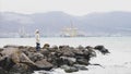 Woman is walking by empty seafront in windy weather with crashing sea waves