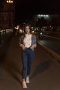Young woman walking on night street. Stylish attractive girl in denim jacket, evening city. Vertical frame Royalty Free Stock Photo