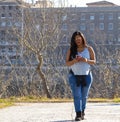 Young woman walking in a park while typing a message on her cell phone Royalty Free Stock Photo