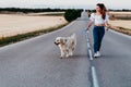 young woman walking by the road with her golden retriever dog at sunset. Pets outdoors Royalty Free Stock Photo