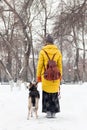 Young woman is walking in a snowy winter park with her dog. Back view Royalty Free Stock Photo