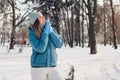 Young woman walking in snowy winter park wearing blue coat. Girl enjoys landscape wearing hat and mittens Royalty Free Stock Photo