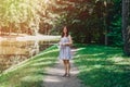 Young woman walking in the summer park. Woman in a green park near the pond. Beautiful woman in a colored sundress Royalty Free Stock Photo